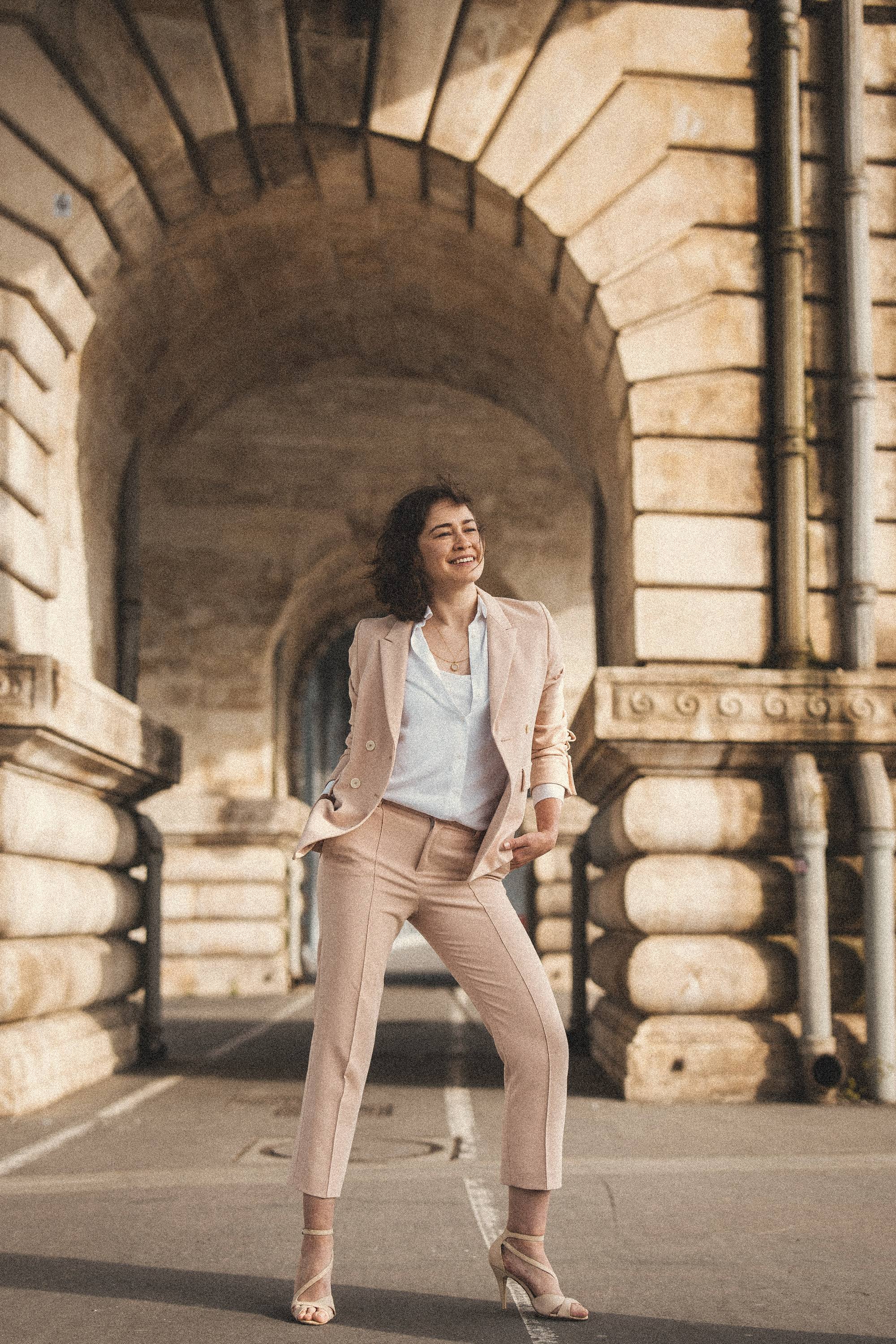 Aliya standing under a stone arch in Paris, full length