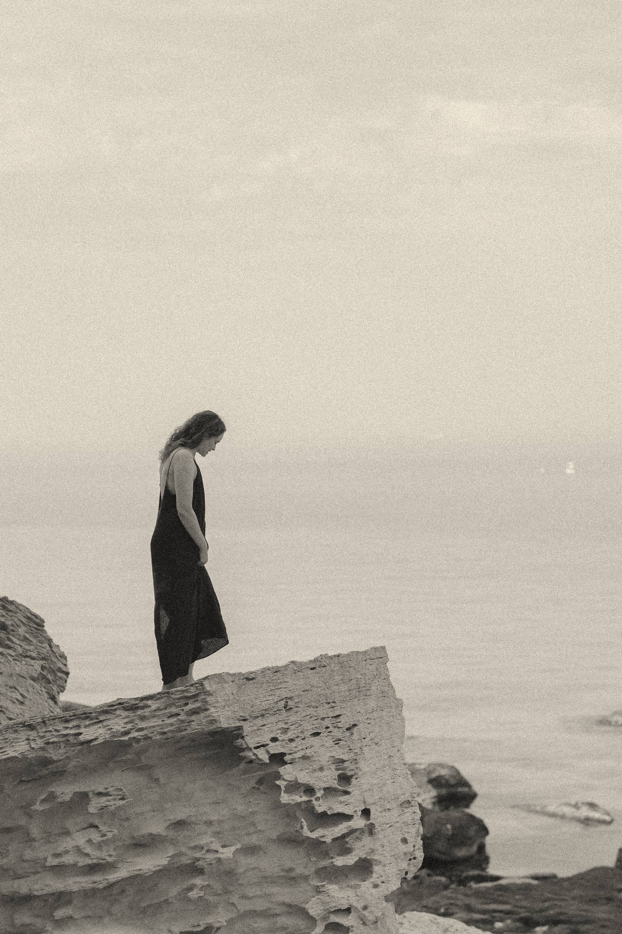 Aliya standing on the rocks by the sea, far away
