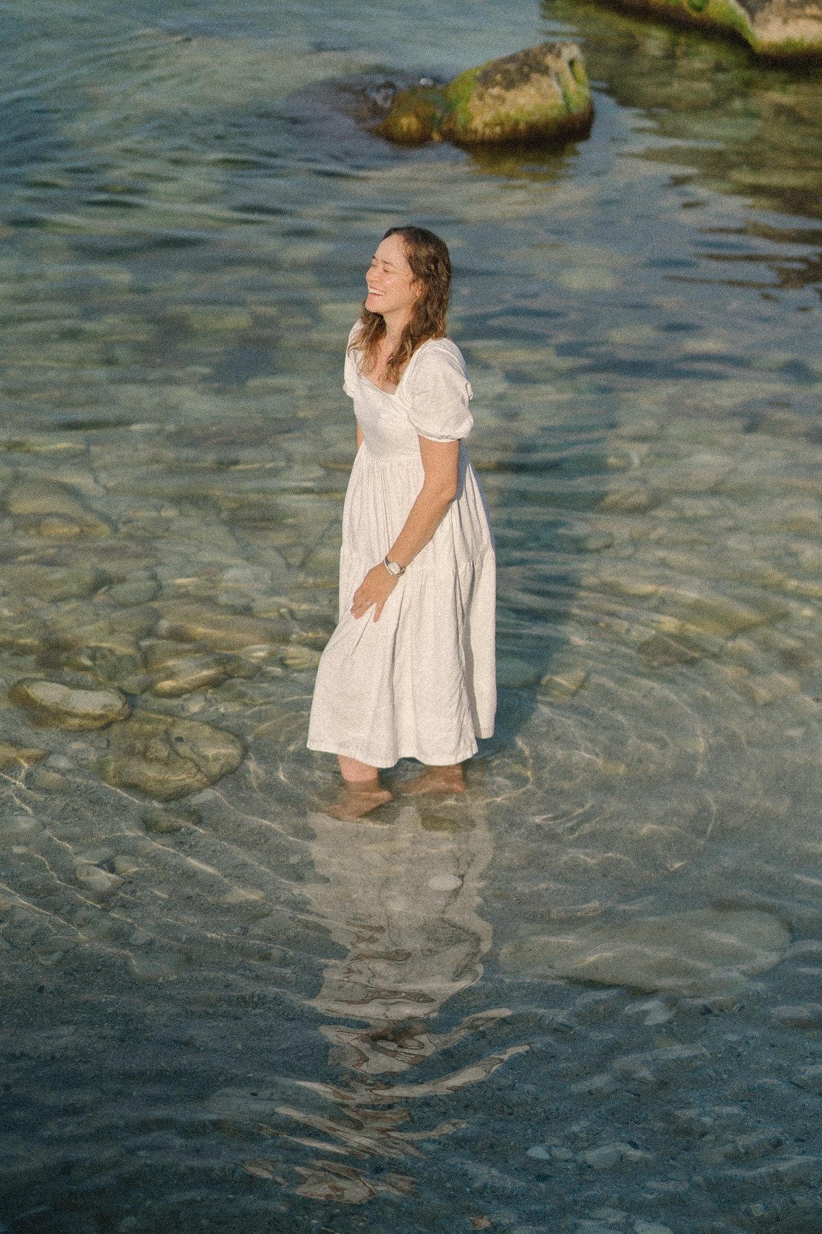 Aliya standing in clear sea water in a white dress